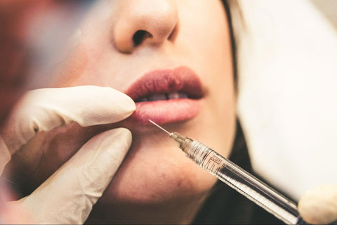 A closeup view of a syringe inserted into a woman’s lips.