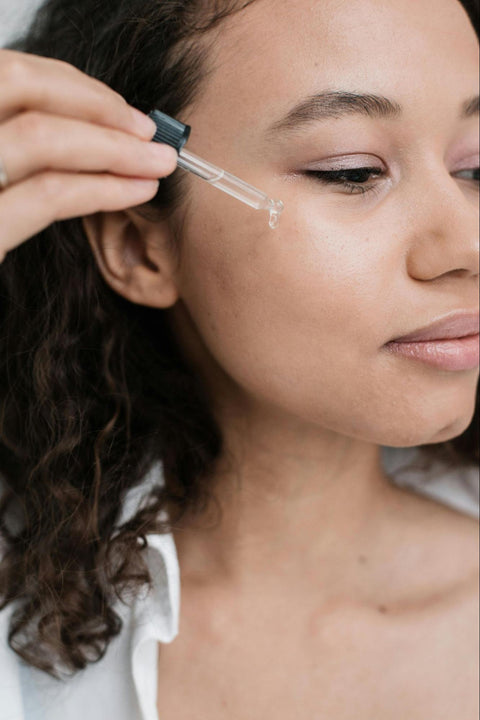 A woman uses a dropper to dispense serum onto her face.