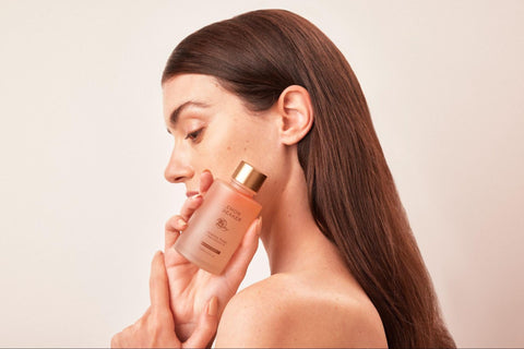 A woman with long dark hair and healthy skin holding up a bottle of Lemon & Beaker toner.