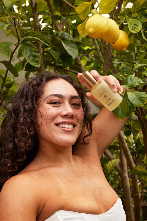 Woman with radiant skin holding Lemon & Beaker's Foaming Deep Cleanser in a natural environment.